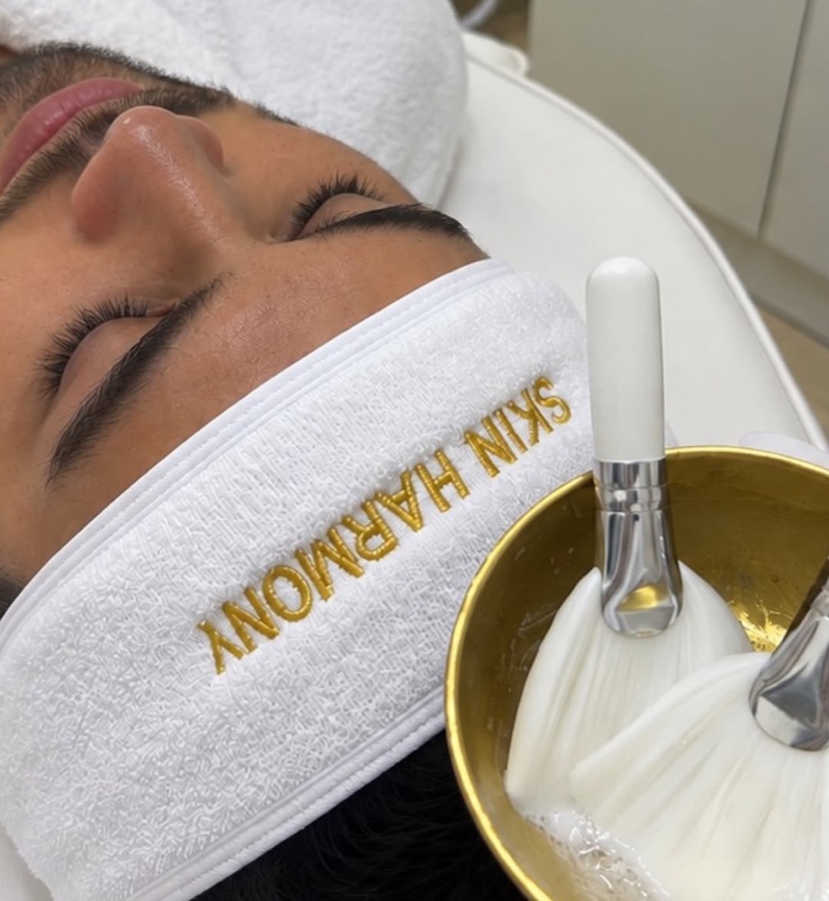 Cliente en limpieza facial con banda bordada Skin Harmony y un cuenco dorado con brochas.